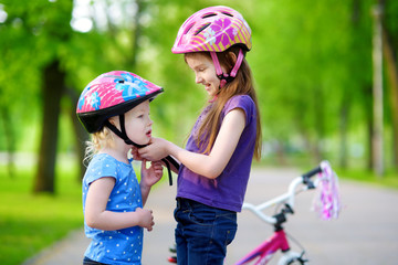 Adorable girl helping her sister to put a bicycle helmet on