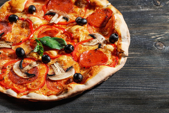 Close-up view of  ITALIAN PIZZA on wooden table. True hot tasty PIZZA with salami, mushrooms, basil, olives, pepper and cheese. Nice for menu Pizzeria. High quality  
