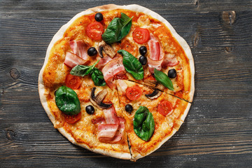 Top view of Italian rustic PIZZA mushrooms, basil, tomato, olives and cheese. Cut off a piece and pushed. Dark wooden table background. Look as Prosciutto, Capricciosa, Funghi, Cotto PIZZA.