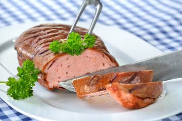 Ofenfrischer bayerischer Leberkäse auf weißer Porzellanplatte auf weiß-blau kariertem Tischtuch - Bavarian meat loaf on a white plate served on a table with a white and blue checkered tablecloth