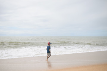 Back view of boy walking along the beach outside during sunset