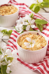 Crumble with strawberry and black currant on a white wooden background with flowering branches of apple trees 
