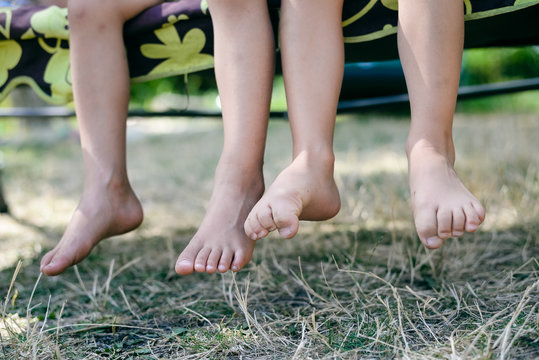 Outdoor picture of two children legs barefoot. Closeup of happy kids sitting on sunny countryside.