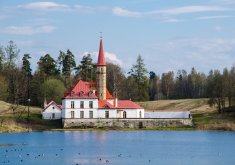 Ancient small castle with white walls and red roof. Sunny summer day, blue sky.  Lake foreground. 