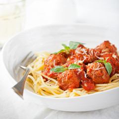 Meatballs in tomato sauce and fresh basil with spaghetti on a white plate