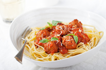 Meatballs in tomato sauce and fresh basil with spaghetti on a white plate