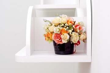 Artificial flowers on white wooden shelves. Artificial rose flower in flowerpot.