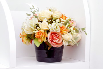 Artificial flowers on white wooden shelves.artificial rose flower in flowerpot.