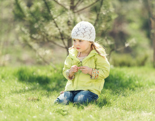 smiling little girl in yellow coat sitting on a lawn in a park