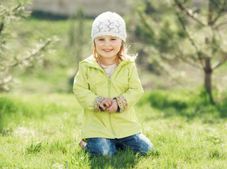 smiling little girl in yellow coat sitting on a lawn in a park