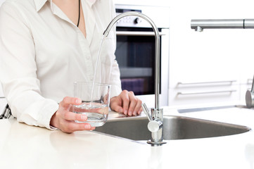 Pouring fresh water from ozone filter into the glass by woman in kitchen