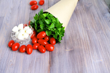 Wet fresh basil (herbs) in the cone of paper, cherry tomatoes and mozzarella cheese on a wooden table