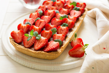 Homemade tart with strawberries and strawberry curd decorated mint leaves on white wooden background