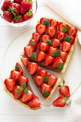 Homemade tart with strawberries and strawberry curd decorated mint leaves on white wooden background