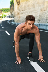 Obraz premium Sports. Healthy Athletic Man With Fit Muscular Body In Starting Position For Running On Road. Handsome Runner Ready To Start Sprint Race. Fitness Model Training Outdoors In Summer. Workout Concept