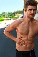 Obraz premium Stomach Ache. Closeup Portrait Of Athletic Man With Fit Muscular Body Touching Belly, Suffering From Abdominal Pain. Handsome Fitness Runner Feeling Bad After Running Outdoors. Sport Injury Concept