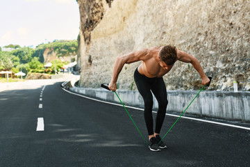Fitness Exercise. Athletic Man With Fit Muscular Body Exercising During Outdoor Workout. Handsome Athlete Model Doing Expander Exercises And Training On Road In Summer. Sport, Active Lifestyle Concept