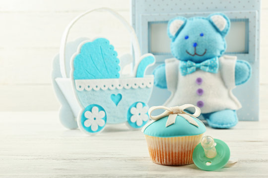 Tasty cupcakes with bow and baby shoes, decorative baby carriage and photo album  on color background