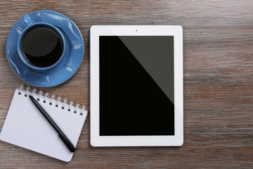 Tablet with cup of coffee and notepad on wooden table