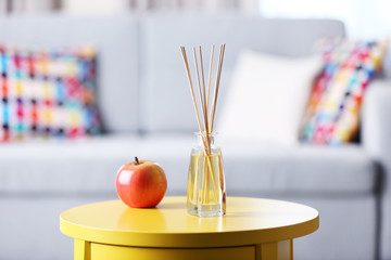 Handmade reed freshener with red apple on yellow table in living room, close up