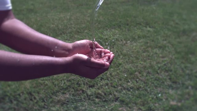 Hands of African American child capturing water in bright sunshine.