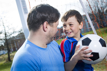 man with with child playing football on football pitch