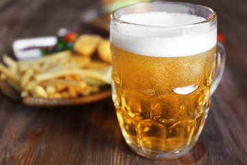 Glass mug of light beer with snacks on dark wooden table, close up