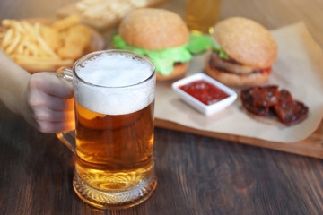 Glass mug of light beer with snacks on dark wooden table, close up