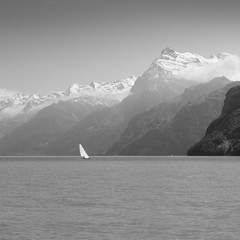Grandiose mountain landscape. Mountain tops in the snow. White sail on a romantic lake. Black and white.