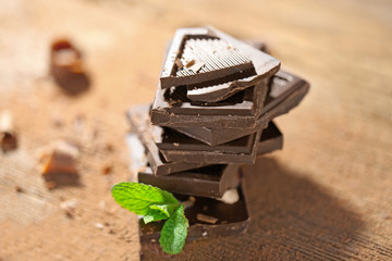 Stack of black chocolate pieces with fresh mint on wooden table