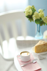 Cup of coffee with cake on white table in light interior