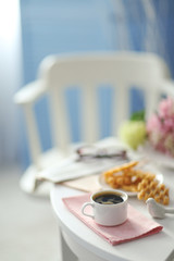Cup of coffee with wafers on white table in light interior