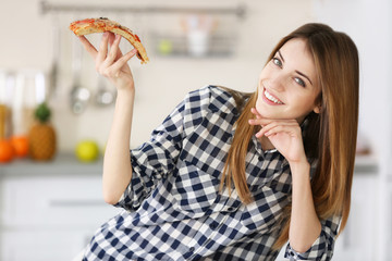 Happy young woman eating slice of hot pizza at home