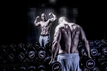 Fototapeta na wymiar Bodybuilder man in front of mirror posing with dumbbell