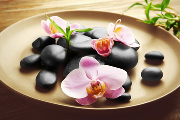 Fototapeta na wymiar Spa stones and orchid flowers in plate on wooden table closeup