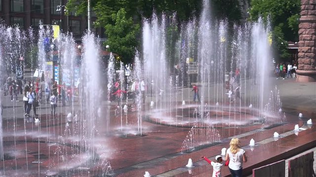 Hot summer weekend in city, families walking near fountain, children playing
