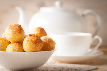 Fresh homemade coconut cookies in white bowl on wooden background with white porcelain teapot and cup