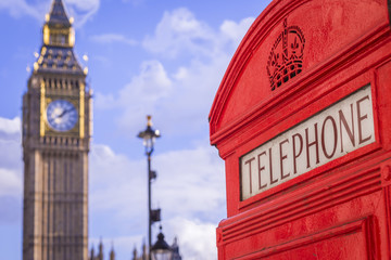 Classic red British telephone box with the Big Ben at background on a sunny afternoon with blue sky and clouds - London, UK