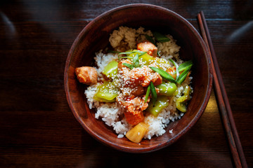 Asian cuisine - rice in sauce with stir fried vegetables, pineapple and salmon. Wooden bowl with...