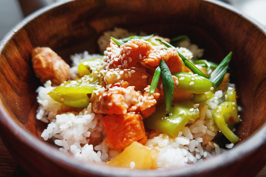 Asian cuisine - rice in sauce with stir fried vegetables, pineapple and salmon. Wooden bowl with chopsticks. 