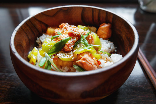 Asian cuisine - rice in sauce with stir fried vegetables, pineapple and salmon. Wooden bowl with chopsticks. 