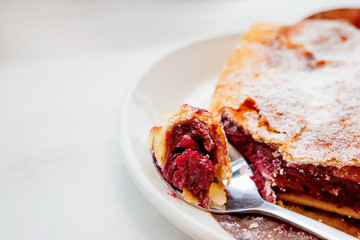 Cherry strudel on a saucer with a spoon. Piece of fresh tasty dessert with berries.