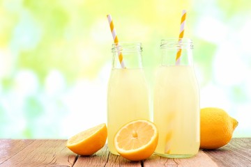 Two bottles of cold lemonade with lemon slices and straws with de-focused outdoor background