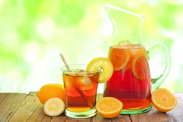 Pitcher of iced tea with glass and lemon slices against a defocused outdoors background