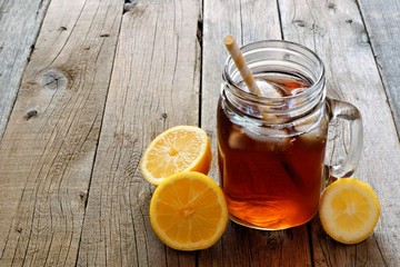 Mason jar glass of cold iced tea with lemon slices on a rustic wood background