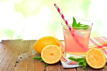 Glass of cold pink lemonade with lemon slices and mint, on wood with outdoors background