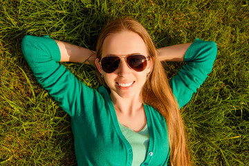 Top view of pretty young woman in glasses lying on grass