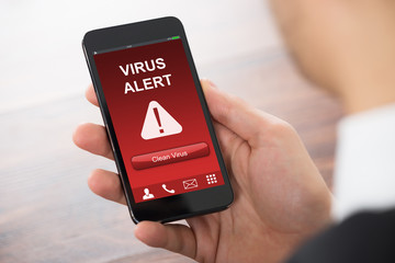 Businessman Holding Mobile Phone With Virus Alert