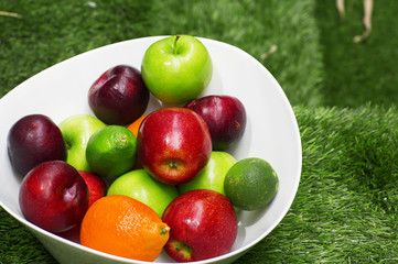 Green and red apples in a big white dish. The fruit bowl filled with assorted fresh fruits. 