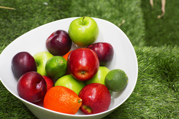 Green and red apples in a big white dish. The fruit bowl filled with assorted fresh fruits. 